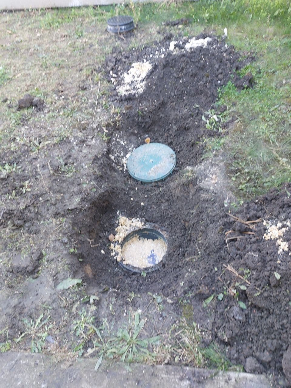 Két kerti tisztítóakna fedele a földben, körülötte feltört talaj