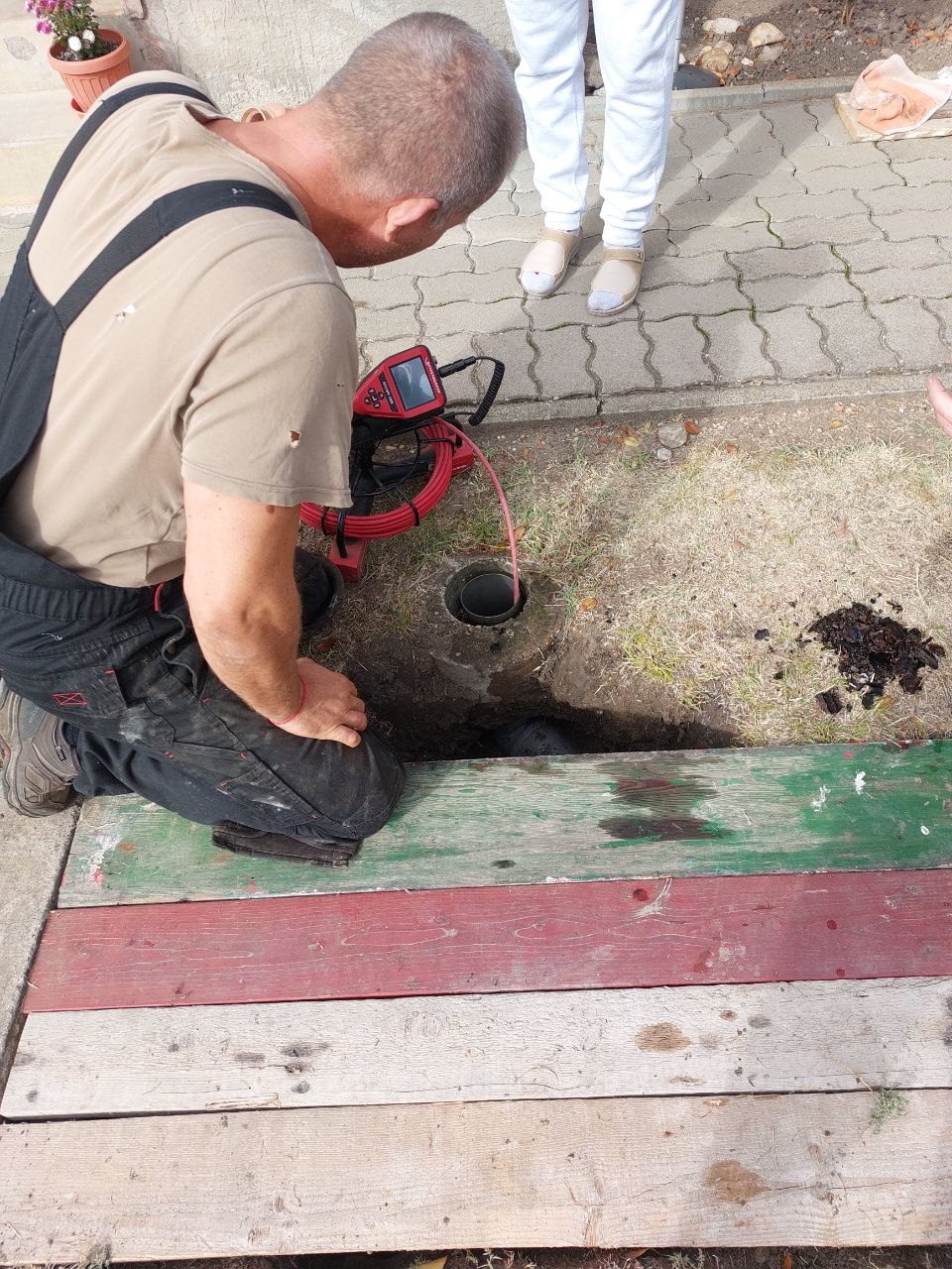 Szerelő térdelve a földbe épített nyílásnál az udvaron, mellette a gépi spirálos készülék